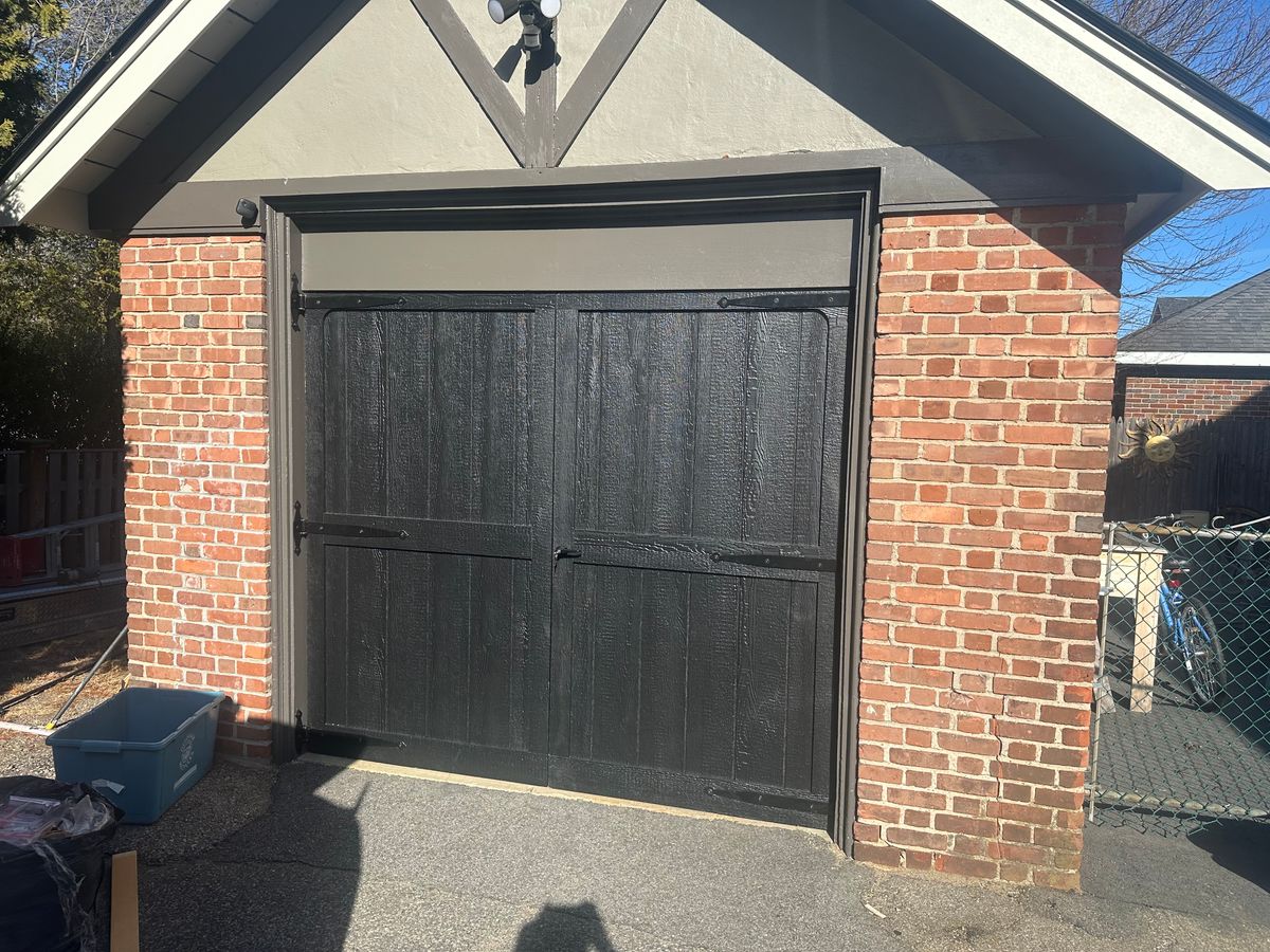Black carriage-style garage door with decorative hardware on brick Tudor-style garage