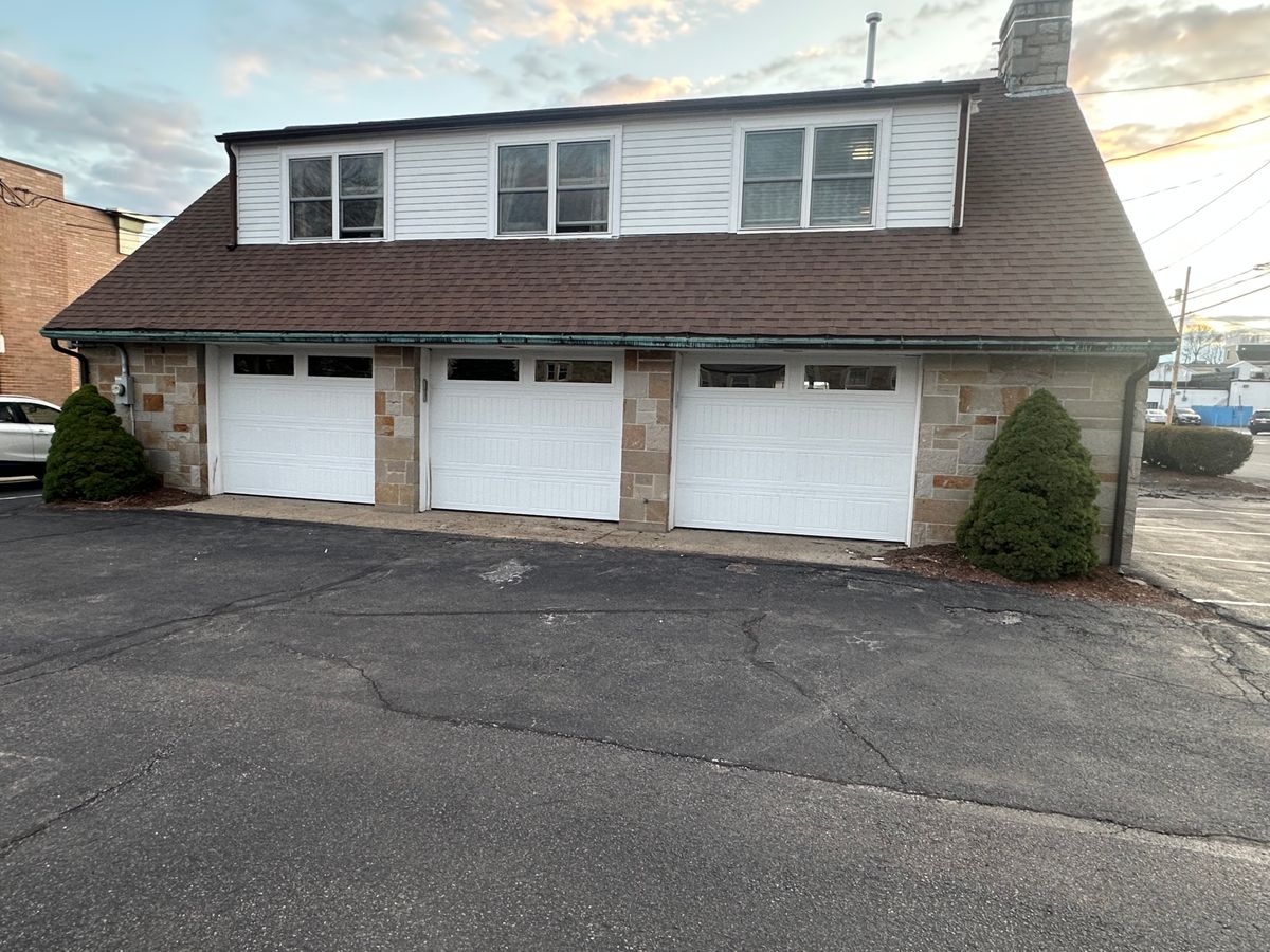 Triple white garage doors with transom windows on stone-faced commercial building
