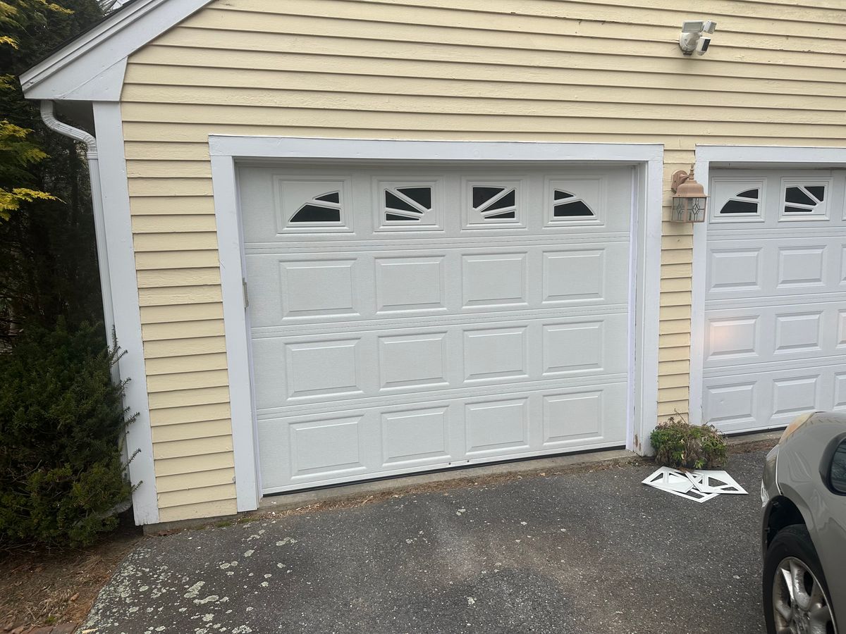 White raised-panel garage door with sunburst windows on yellow colonial home